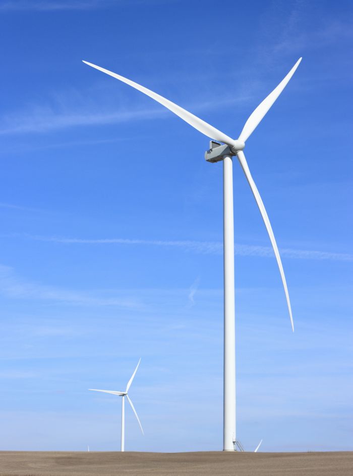 Wind turbines standing tall against a vibrant blue sky in an open countryside setting.