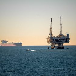 Offshore oil platform with container ship in tranquil sea during daytime.
